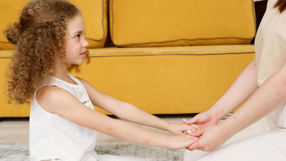 Niña tomada de las manos con un adulto, en un gesto de contención