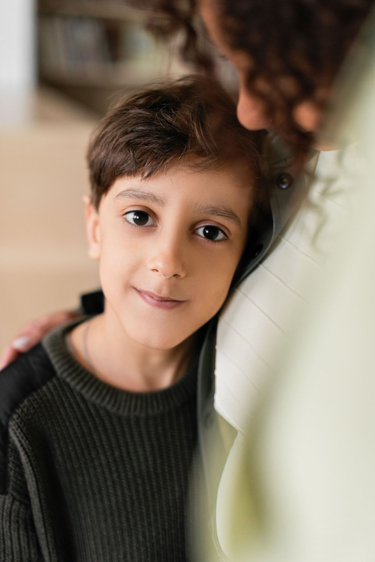 Niño sonriendo apoyado en el hombro de un adulto, en un momento de confianza y calma